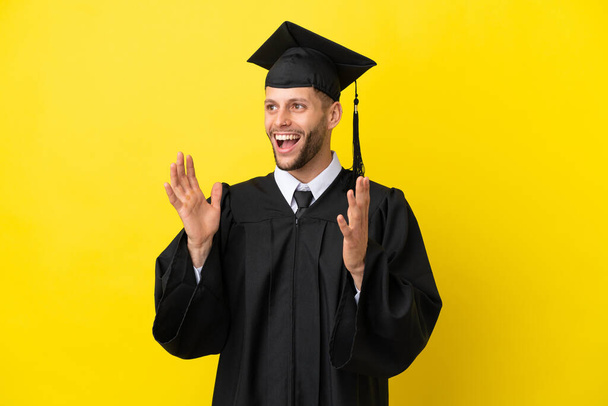 Genç üniversite mezunu beyaz bir adam sarı arka planda şaşırmış bir yüz ifadesiyle izole edilmiş. - Fotoğraf, Görsel