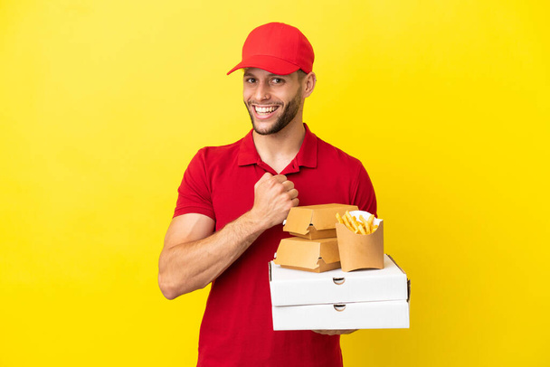 dostawca pizzy podnosząc pudełka po pizzy i hamburgery na odosobnionym tle świętując zwycięstwo - Zdjęcie, obraz