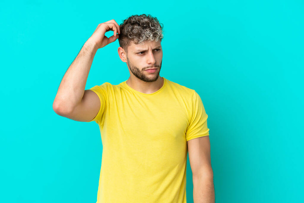 Young handsome caucasian man isolated on blue background having doubts while scratching head - Fotoğraf, Görsel