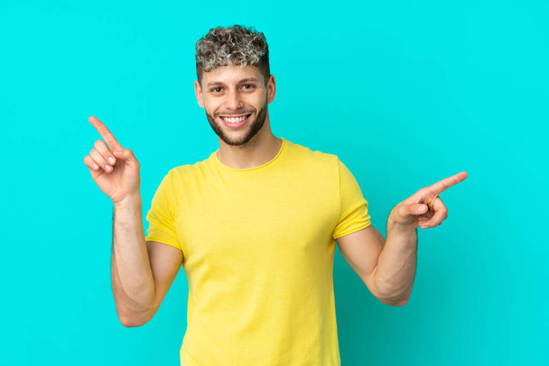 Fiatal jóképű fehér férfi elszigetelt kék háttér mutató ujját a laterals és boldog - Fotó, kép