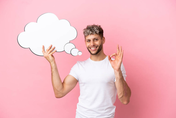 Young handsome caucasian man isolated on pink background holding a thinking speech bubble and doing OK sign - Фото, зображення