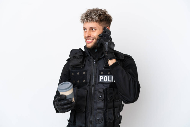 SWAT caucasian man isolated on white background holding coffee to take away and a mobile - Fotografie, Obrázek