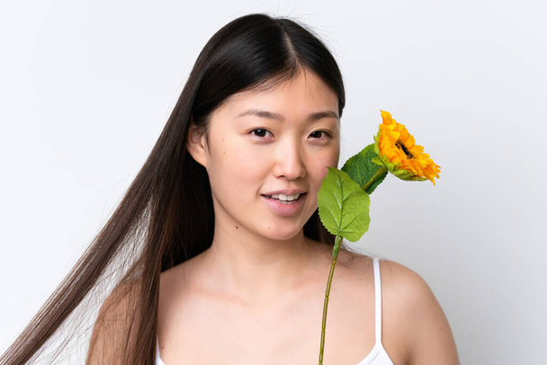 Młoda Chinka odizolowana na białym tle trzymająca słonecznik podczas uśmiechu. Portret z bliska - Zdjęcie, obraz