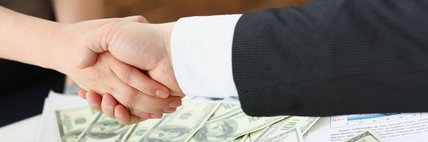 Close-up of businesspeople shake hands over bunch of dollar banknotes, transaction of powers. People agreed on price. Business, money, investment concept - Photo, Image