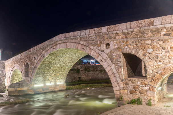 The Old Stone Bridge crosses the Prizrenska Bistrica river at night. - Foto, Imagen