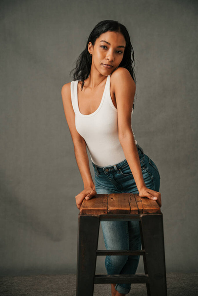 Attractive African American female posing on a chair in her jeans wearing her white T shirt. High quality photo - Zdjęcie, obraz