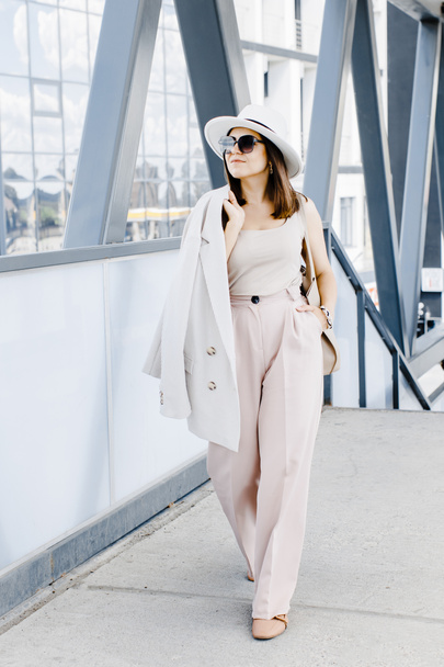 Beautiful brunette businesswoman wearing suit and white hat, walking on the street. Beautiful woman walking to the meeting - 写真・画像
