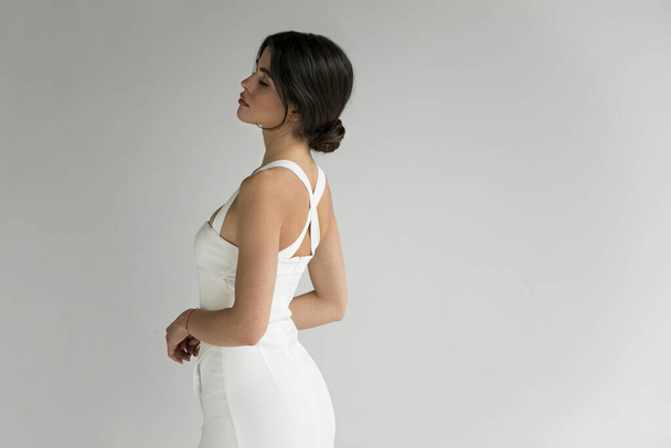 Rear view of young woman in white dress posing in studio, isolated grey background. - Foto, Bild