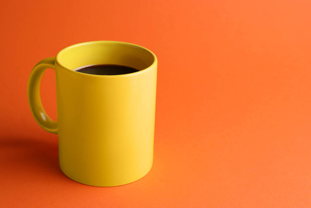Yellow mug of freshly brewed hot coffee on orange background, space for text - Photo, Image