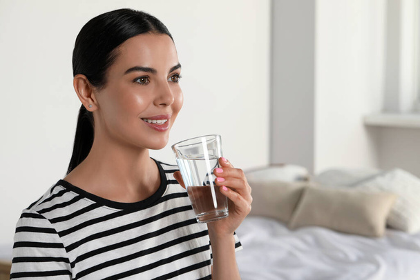 Young woman with glass of water indoors, space for text. Refreshing drink - Photo, image
