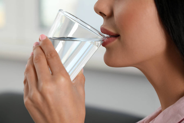 Mujer joven bebiendo agua en el interior, primer plano. Bebida refrescante - Foto, Imagen