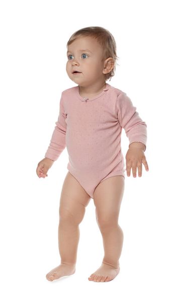 Cute baby girl in pink bodysuit learning to walk on white background - Фото, зображення