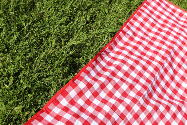 Checkered picnic tablecloth on fresh green grass, closeup. Space for text - Foto, Imagem