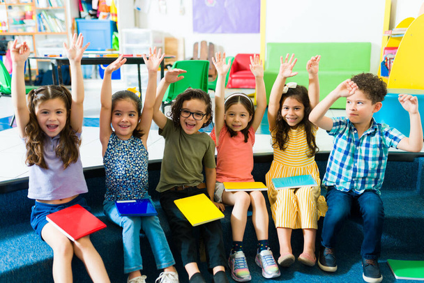 Cheerful preschool children raising their hands and having fun while learning in kindergarten  - Photo, Image
