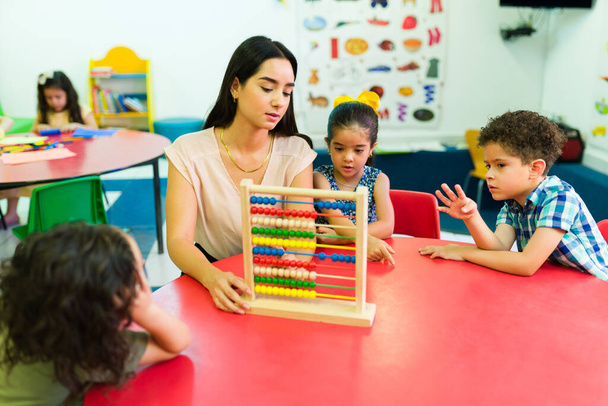 Leraar kleuterschool met behulp van een abacus tijdens het onderwijs van de nummers en om te tellen om hun kleuterschool jongens en meisjes - Foto, afbeelding