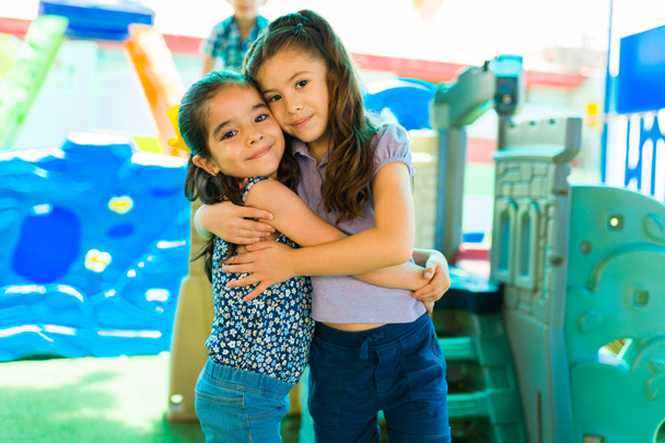 Beautiful girl friends hugging and smiling while playing in the playground during kindergarten recess - Foto, imagen
