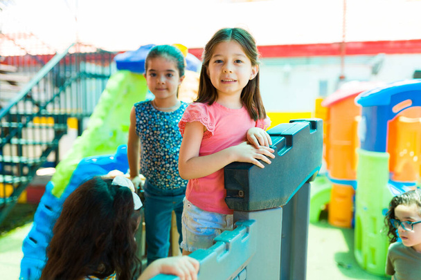 Кавказька дівчинка посміхається, граючи з однокласниками на дитячому майданчику під час перерви дошкільних занять. - Фото, зображення