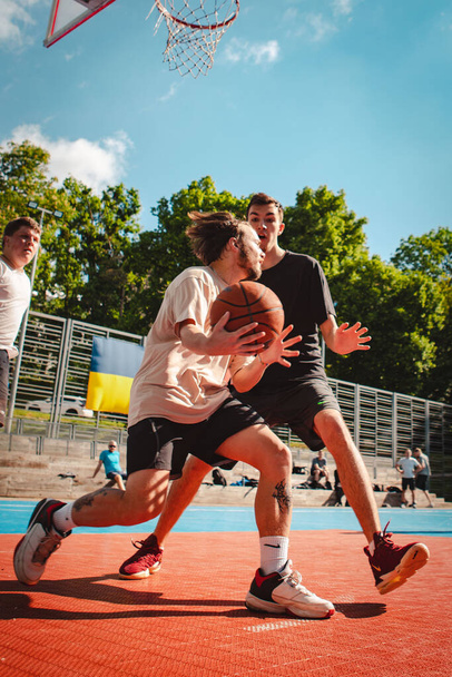 Lviv, Ukraine - May 28, 2022: men playing basketball outdoors sunny summer day - Фото, зображення