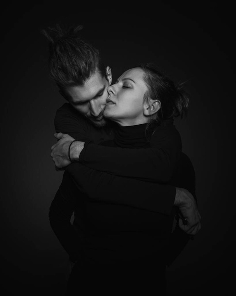 Love story concept. Portrait of a beautiful couple in love posing at studio over dark background. Monochrome portrait of a passionate couple making funny grimace on face laughing playful - Zdjęcie, obraz