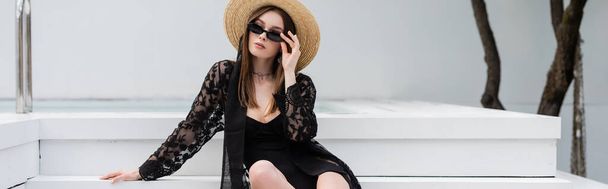 Stylish woman in swimsuit and sun hat holding sunglasses near pool, banner  - Foto, immagini