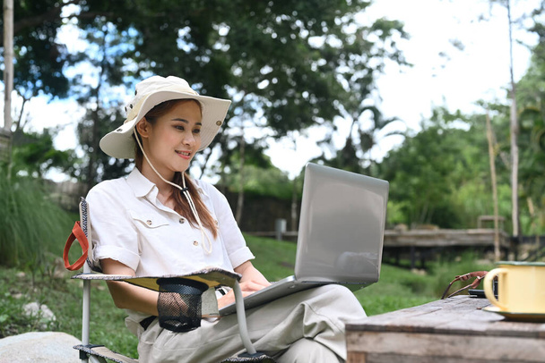Junge Frau sitzt in Bachnähe und benutzt Laptop. Reisen, Abenteuer in der Natur und Urlaubskonzept. - Foto, Bild