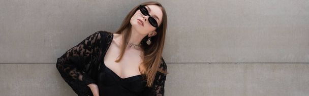 Trendy woman in sunglasses and guipure robe standing near wall, banner  - Foto, Imagen