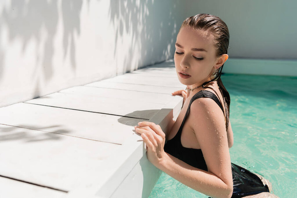 pretty young woman with wet hair and stylish black swimsuit in pool  - Foto, imagen