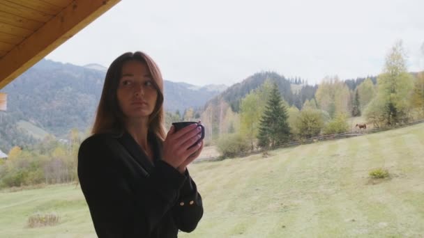 Long-haired beautiful woman holds cup coffee, tea, view mountains, forest, valley. Cloudy, medium shot. Concept of feedback, hotel, good morning, relaxation, enjoyment, nature. High quality 4k footage - Séquence, vidéo