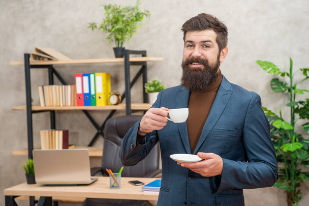 cheerful bearded businessman drinking coffee in the office with copy space, business. - Foto, Bild