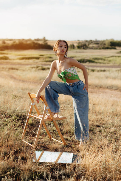 Fashionable young model in boho style clothes on a background of dry grass, field. Female beauty and style concept. Advertisement or clothes sale design. - Φωτογραφία, εικόνα