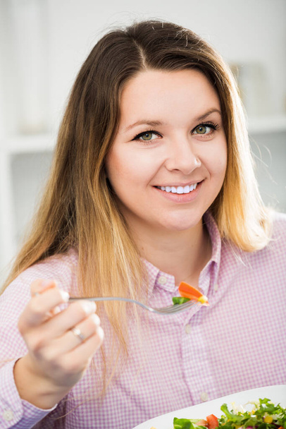 Young smiling woman trying tasty green salad at home. - Valokuva, kuva
