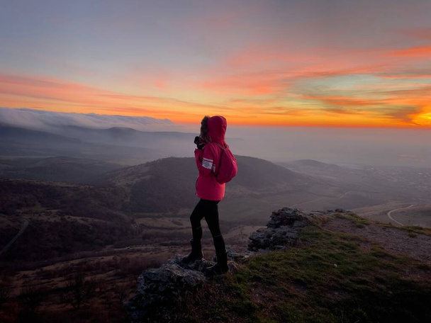 Жінка-ведуча, що стоїть на вершині пагорба і милується заходом сонця взимку
 - Фото, зображення