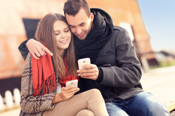 Paar zittend op een bankje en het gebruik van smartphones - Foto, afbeelding