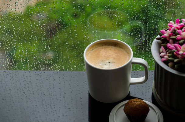 A cup of hot coffee with small cake on table in morning with rain drop on window and green background. Stay home and relaxing concept.	 - Foto, Imagen