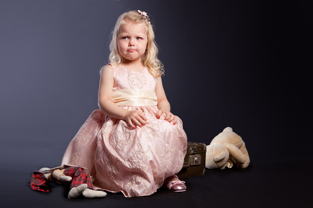 Curly girl in pink dress sitting on old suitcase - Photo, Image