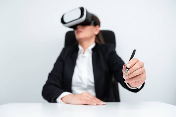 Businesswoman Wearing Virtual Reality Simulator And Holding Pen At Desk. - Фото, изображение