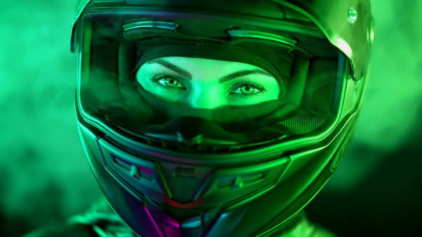 Young female motorcyclist woman in closed motorcycle helmet. Driver biker looking to camera under green colorful neon light with smoke or steam at night. Amazing aesthetic portrait. High quality photo - Foto, imagen