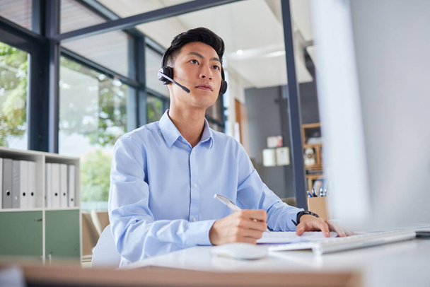 Asian translator or business man with headset looking serious while sitting in office. Accountant checking documents, preparing financial report. Focused call centre agent sitting at his desk. - Foto, afbeelding