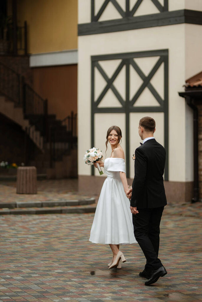 young couple bride and groom in a white short dress walking in the rain - Foto, Bild