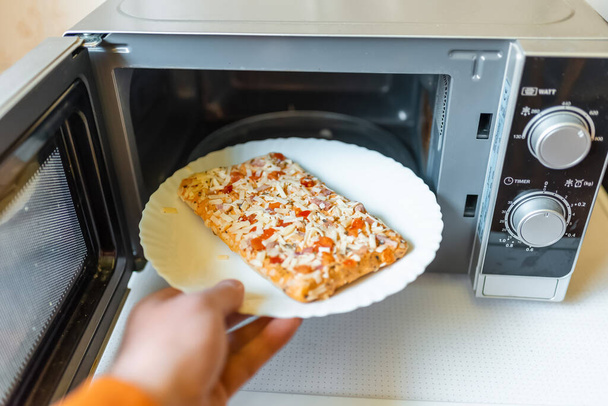 Pizza pequeña congelada sin cocer colocada en la comida microwave.junk, concepto de comida rápida.Vista lateral.Enfoque selectivo. - Foto, Imagen