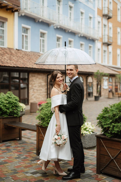 young couple bride and groom in a white short dress walking in the rain - Foto, afbeelding