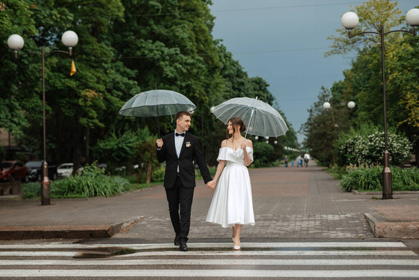 young couple bride and groom in a white short dress walking in the rain - Foto, Imagen