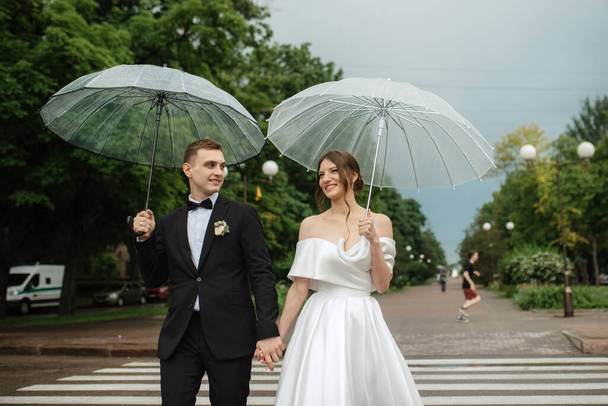 young couple bride and groom in a white short dress walking in the rain - Foto, afbeelding