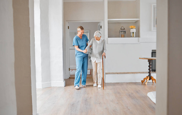 a nurse assisting a senior woman with a walking stick in a retirement home. - Photo, image