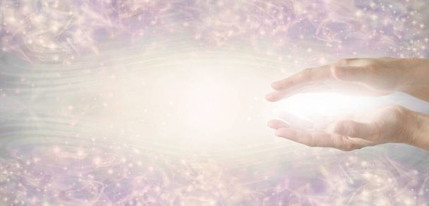 Reiki Healer sending energy distant healing - female cupped hands with white light energy between against a pale grey pink  ethereal  pattern background banner and copy space for messages  - Foto, imagen