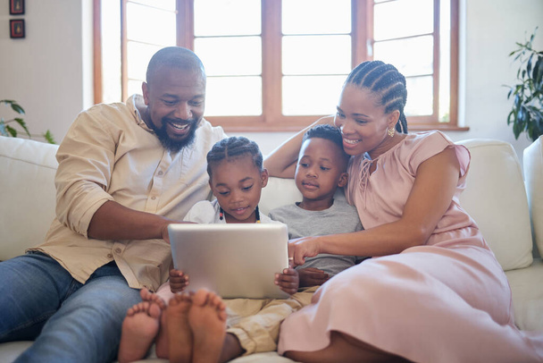 A young african american family sitting on the sofa together and smiling while using a tablet at home. - Foto, imagen