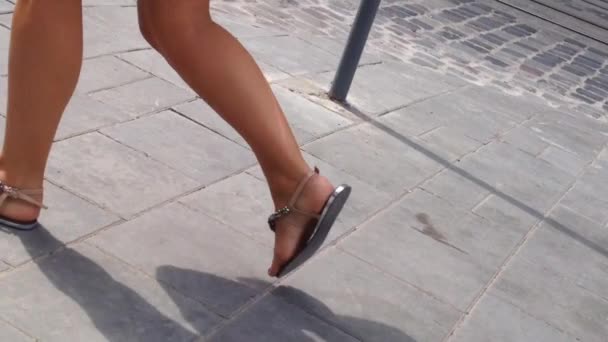 Egy lány cserzett lábai fehér rövidnadrágban és gyönyörű papucsban sétálnak az utcán. - Felvétel, videó