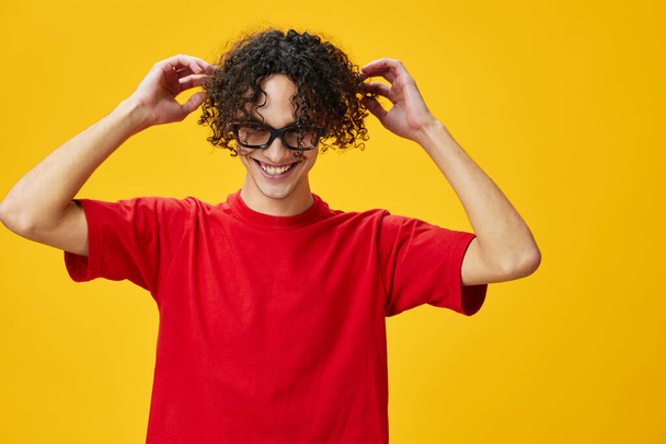 Carino attraente miope giovane studente in rosso t-shirt tenere occhiali divertenti posa isolato su sfondo giallo studio. La migliore offerta con posto libero per la pubblicità. Concetto di Education College - Foto, immagini