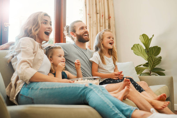 Young carefree caucasian family sitting on the couch and watching a movie together in the lounge at home. Happy little siblings watching tv with their parents. Mom and dad bonding with their girls. - Photo, Image