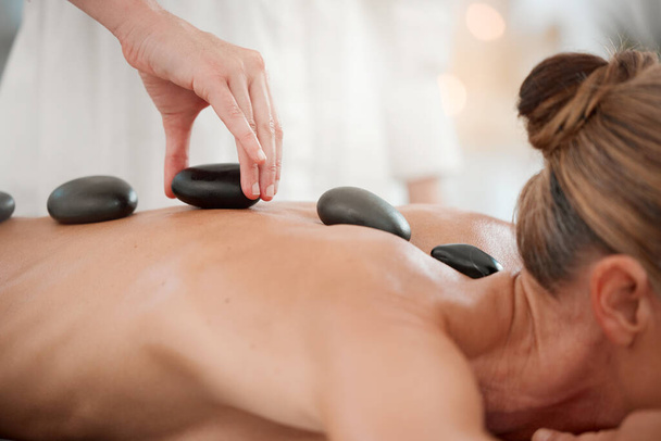 a massage therapist placing hot stones onto a clients back during a treatment. - Photo, image